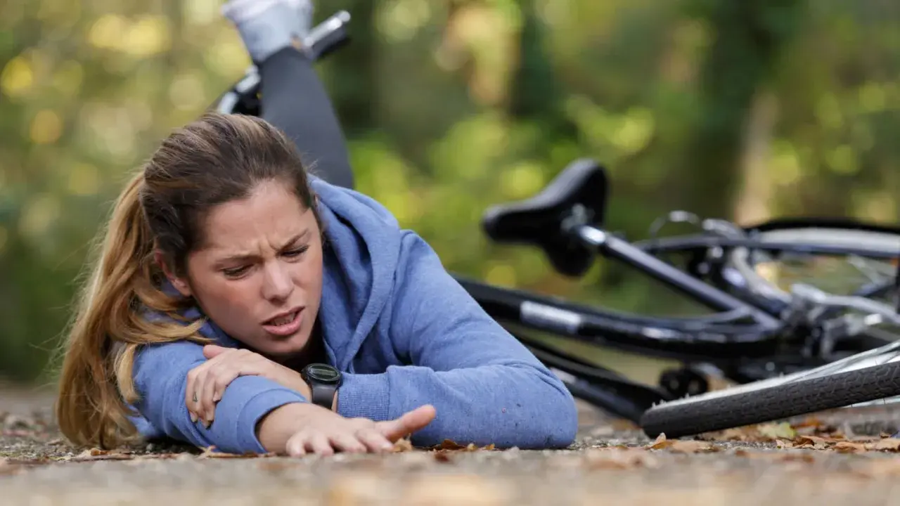 Junge Frau nach einem Sturz auf den Brustkorb, Fahrrad liegt daneben. Sie hält sich den Arm und hat Schmerzen.