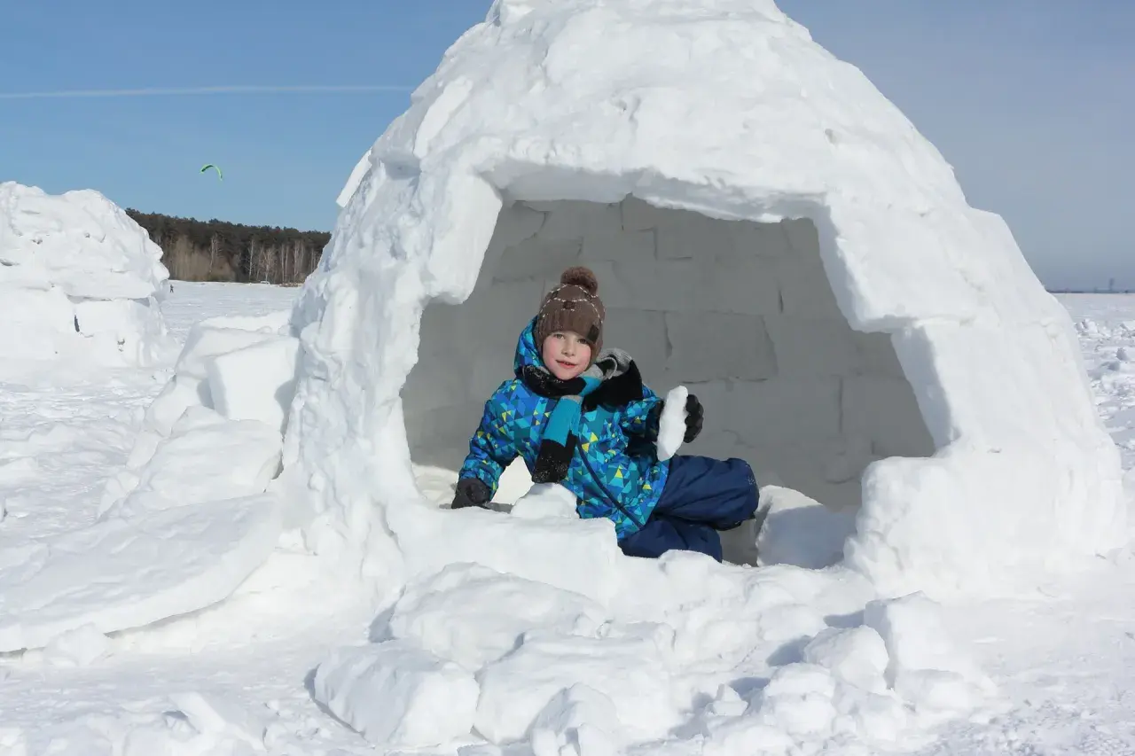 Kind im selbstgebauten Iglu, bereit für Winterabenteuer.