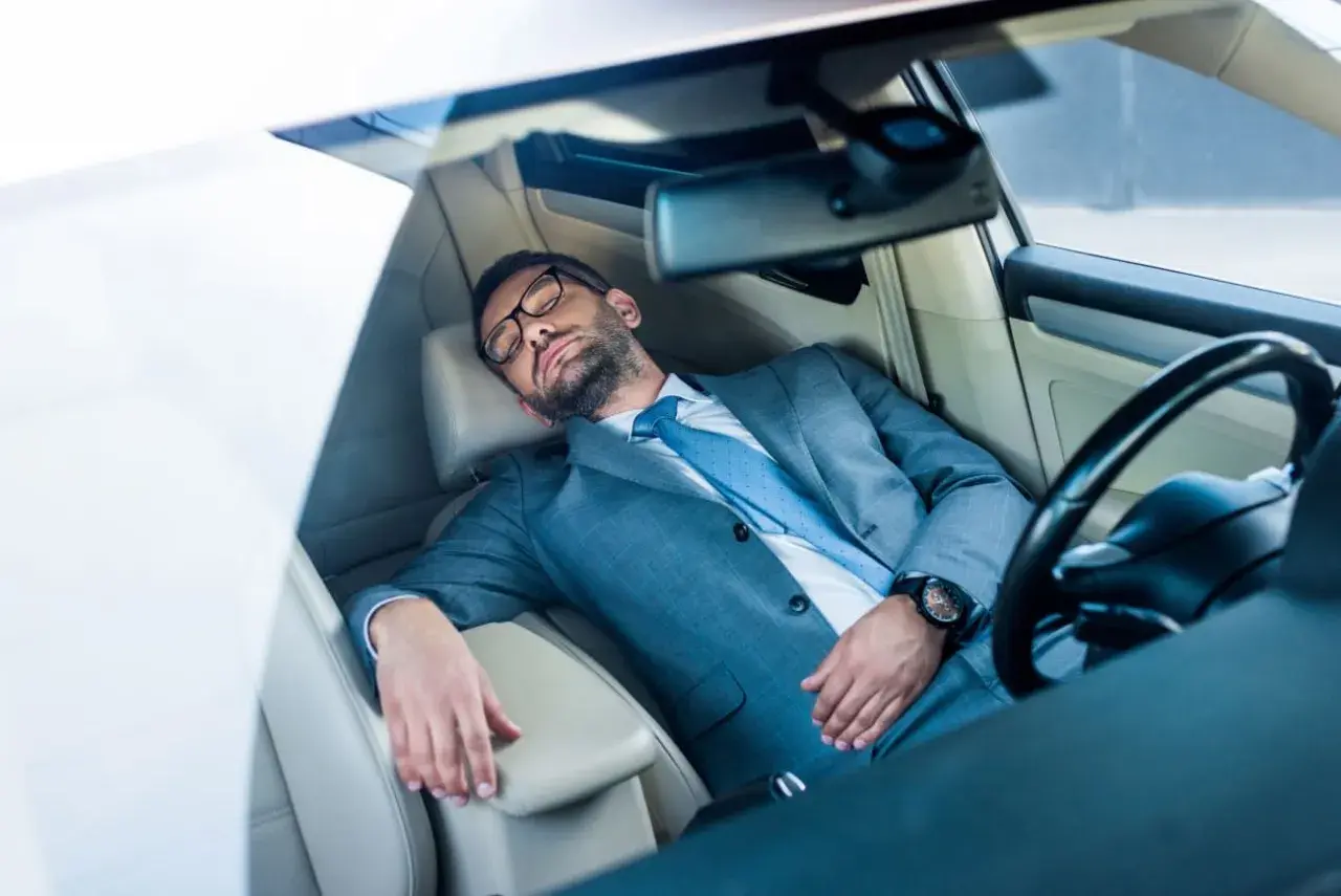 Mann im Anzug schläft im Auto. Ob man in Italien im Auto schlafen darf, ist eine andere Frage.