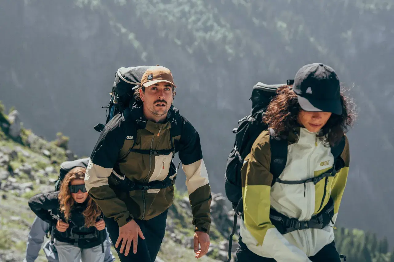 Drei Wanderer mit Rucksäcken steigen einen Bergpfad hinauf. Wie viele Kilometer schafft man wohl in 2 Stunden?