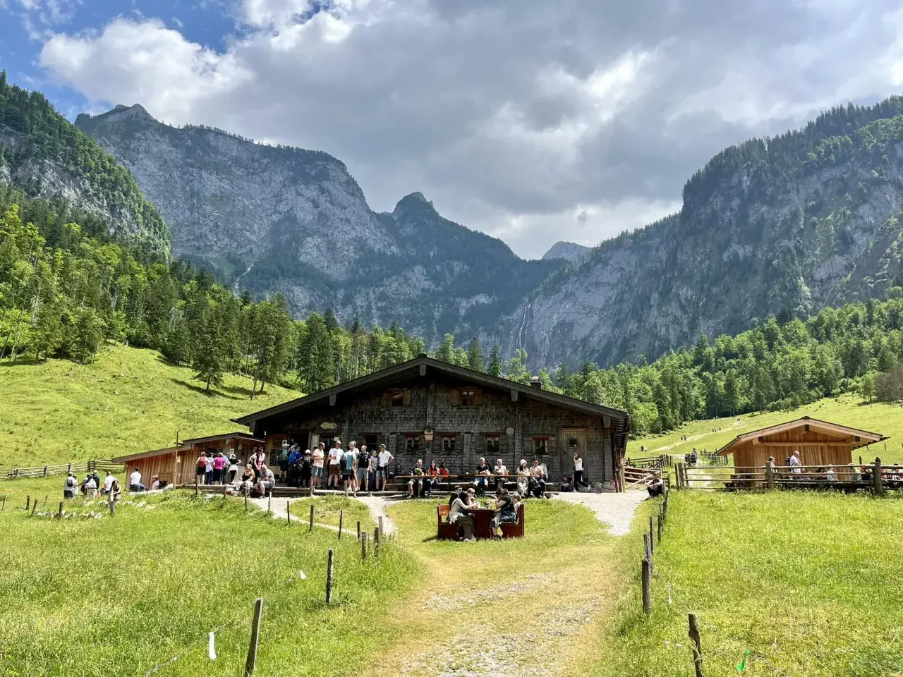 Eine Berghütte mit Gästen vor einer beeindruckenden Bergkulisse, die an ein steinernes Meer erinnert.