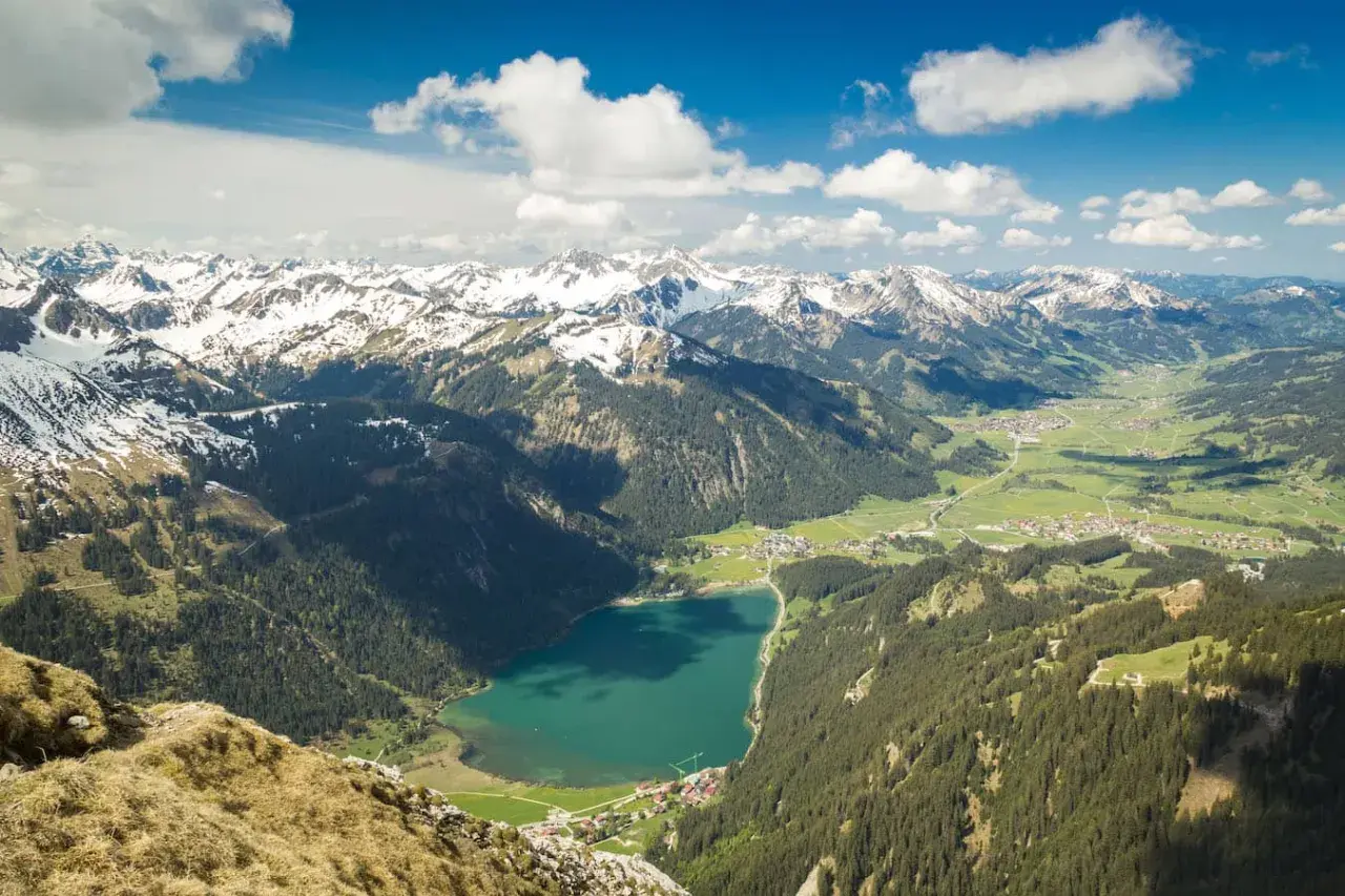 Blick ins Tannheimer Tal mit türkisfarbenem See, grünen Wäldern und schneebedeckten Gipfeln. Entdecken Sie hier Tannheimer Tal Geheimtipps!