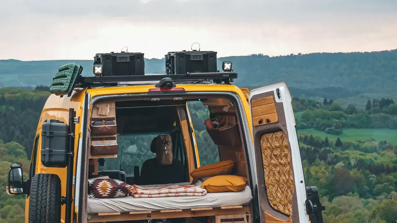 Gelbes Campervan mit gemütlichem Innenraum, bereit für wildcampen in Europa. Dachgepäckträger, Ersatzrad und Stauraum für Abenteuer.