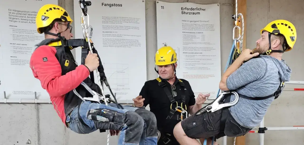 Zwei Männer in gelben Helmen üben das Abseilen nach Schweizer Methode. Einer hängt gesichert in der Luft, der andere erklärt die Technik.