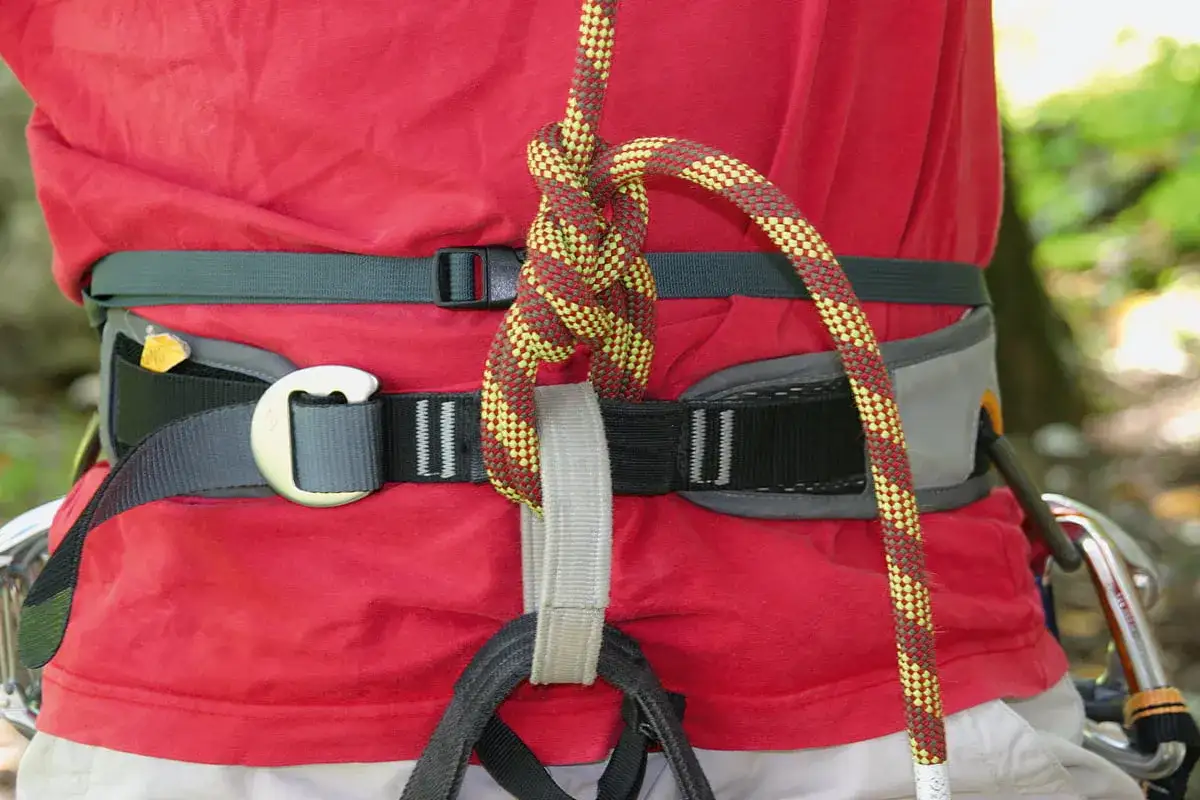Klettergurt aus Seil binden: Ein Bergsteiger knotet das Seil sicher am Klettergurt.