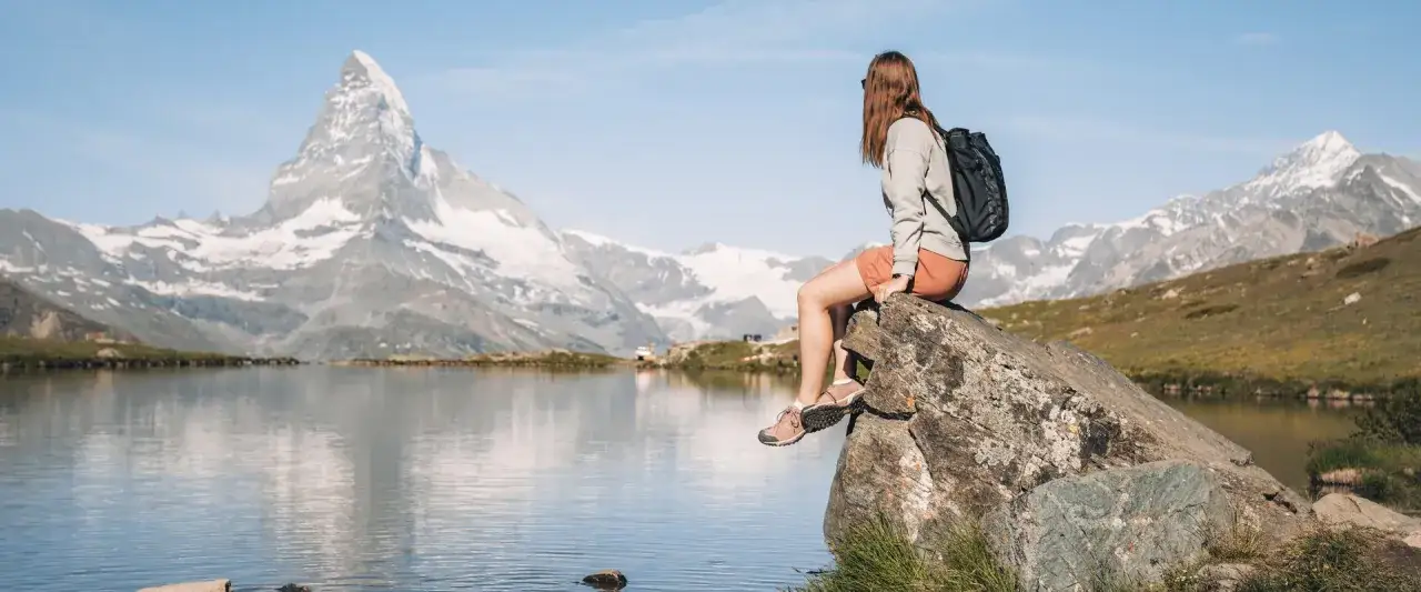 Frau sitzt auf Felsen am See, genießt die Aussicht auf das Matterhorn. Perfekter Moment für eine Matterhorn Wanderung.