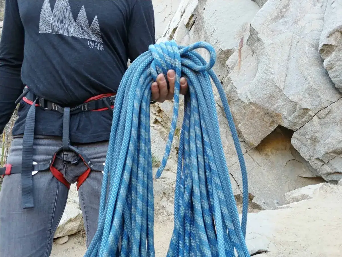 Bergsteiger hält blaues Kletterseil aufwickeln vor Felswand.