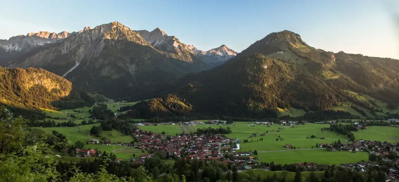 Sonnenbeschienene Berge über Bad Hindelang. Ein idyllisches Dorf liegt eingebettet in grünen Wiesen. Perfekt für eine Wanderung.