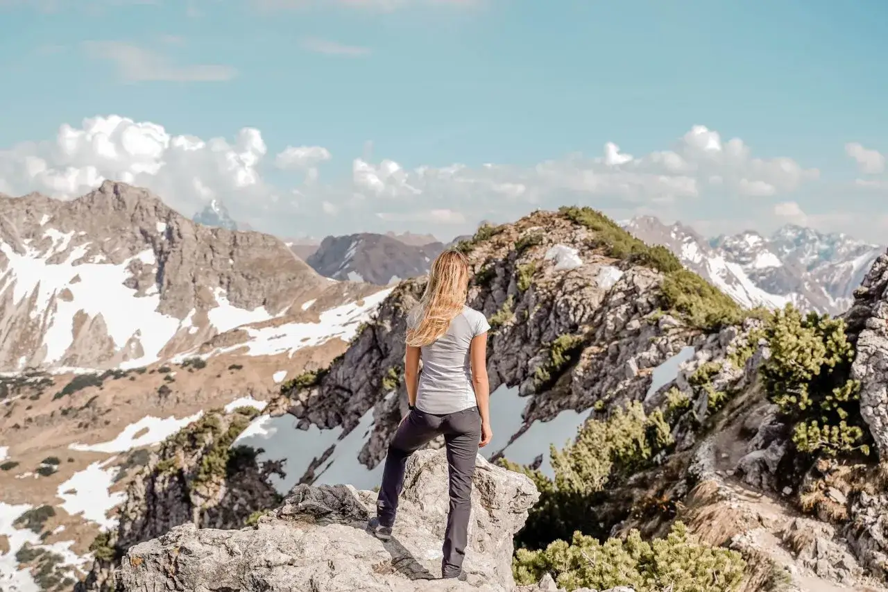 Frau genie&szlig;t die Aussicht nach einer erfolgreichen Rubihorn Wanderung. Schneefelder und felsige Gipfel erstrecken sich bis zum Horizont.