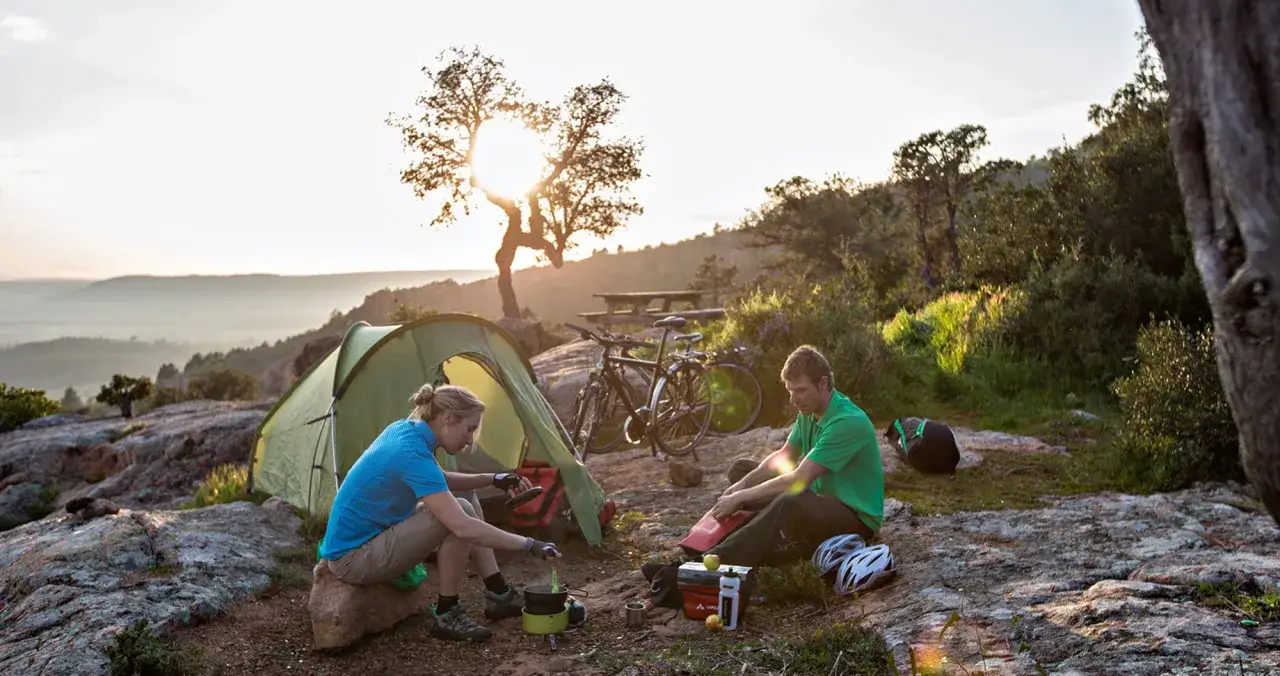 Ein Paar genie&szlig;t das wildcampen Italien bei Sonnenuntergang. Fahrr&auml;der und Zelt stehen bereit f&uuml;r das n&auml;chste Abenteuer.