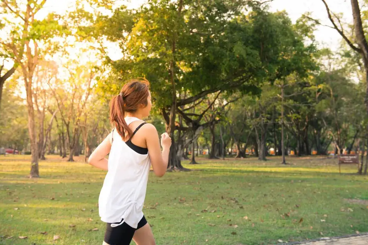 Frau genießt slow jogging im sonnigen Park, umgeben von Bäumen.