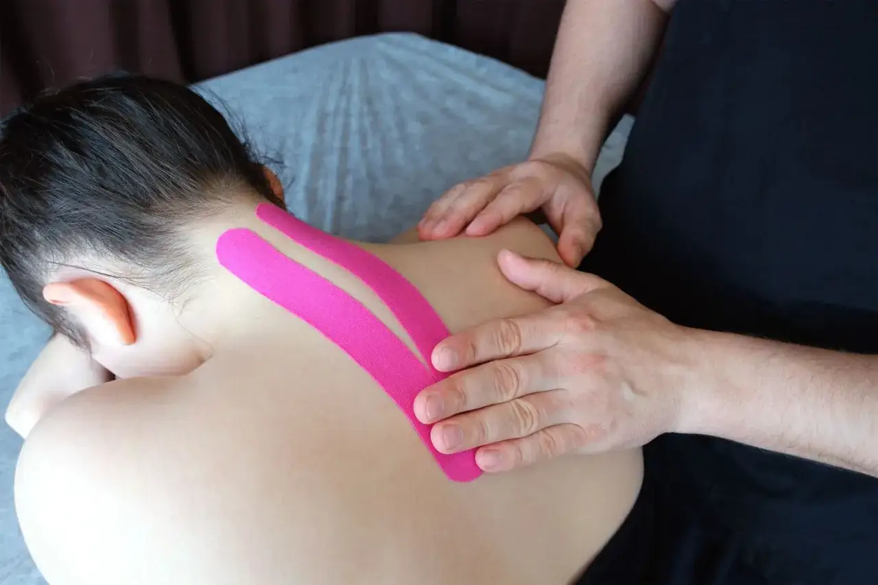 Therapeut legt pinkes Kinesio-Tape an, um das Schulterblatt zu stabilisieren.