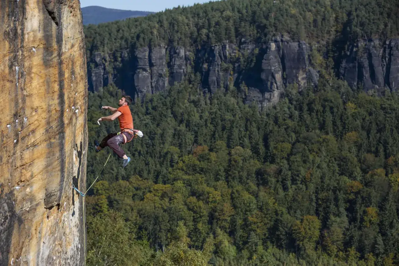 Ein Mann klettert an einer Felswand in Tschechien. Im Hintergrund erstreckt sich ein dichter, grüner Wald.