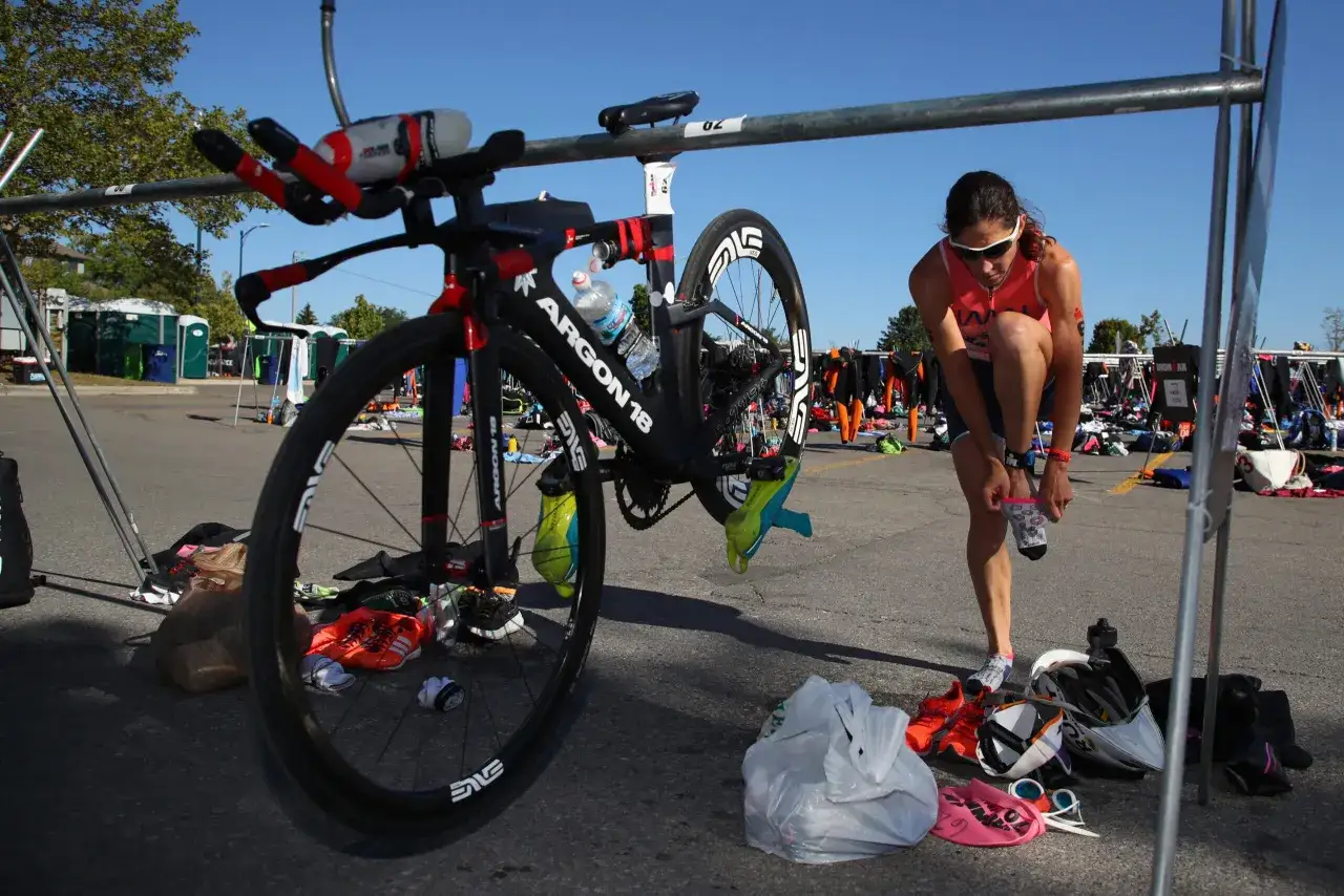 Frau zieht Socken an, bereit für die Triathlon Vorbereitung. Rennrad, Neoprenanzüge und Ausrüstung liegen bereit.