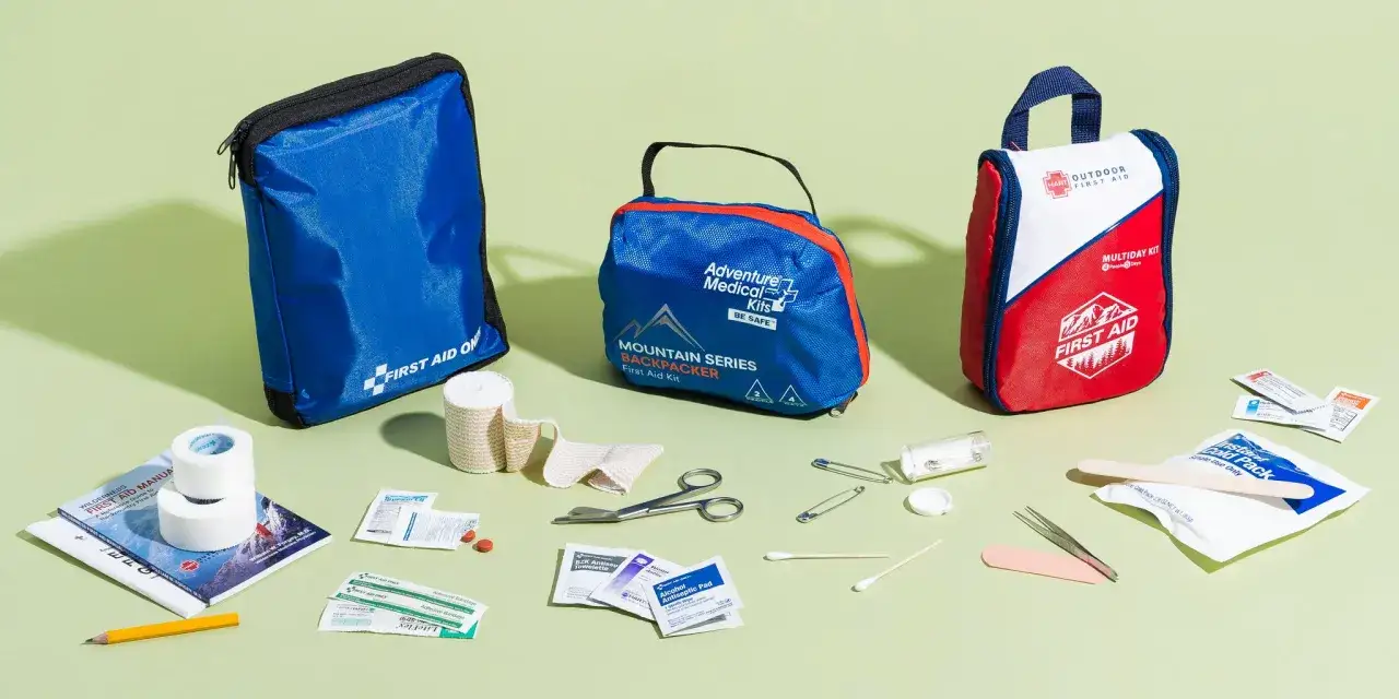 Erste-Hilfe-Sets für unterwegs, darunter ein blaues, ein rotes und ein blau-rotes Set, mit Verbandszeug, Schere und Pflastern für den Kreislauf.