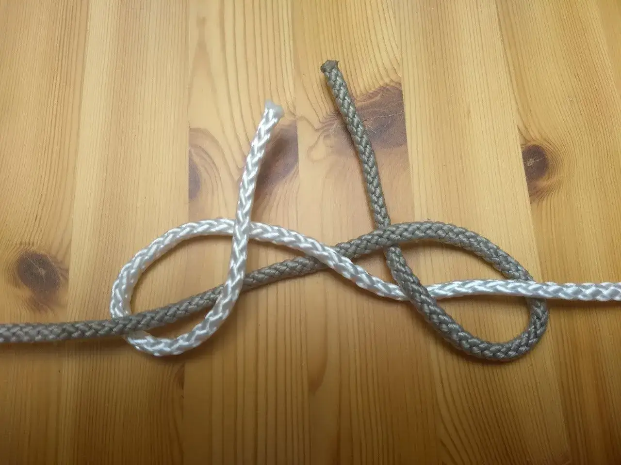 Zwei Seile verbinden ohne Knoten: Ein wei&szlig;es und ein graues Seil werden kunstvoll miteinander verflochten, um eine sichere Verbindung zu schaffen.