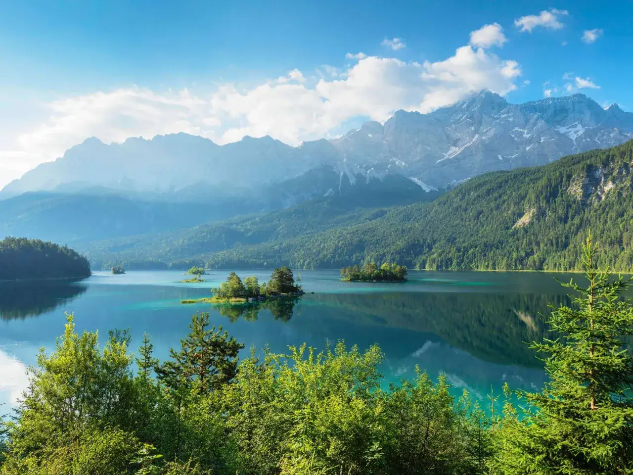 Türkisblaue Seen mit kleinen Inseln, umgeben von grünen Wäldern und majestätischen Bergen. Ein atemberaubender Ausblick, der die Schönheit von Seen in Deutschland zeigt.