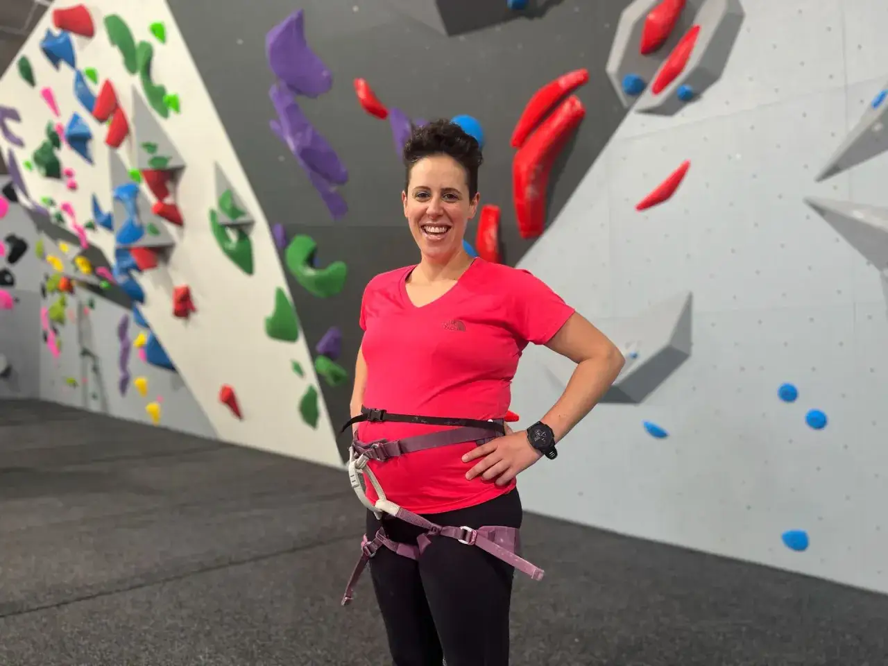 Glückliche Frau mit Babybauch beim Klettern in einer Boulderhalle.