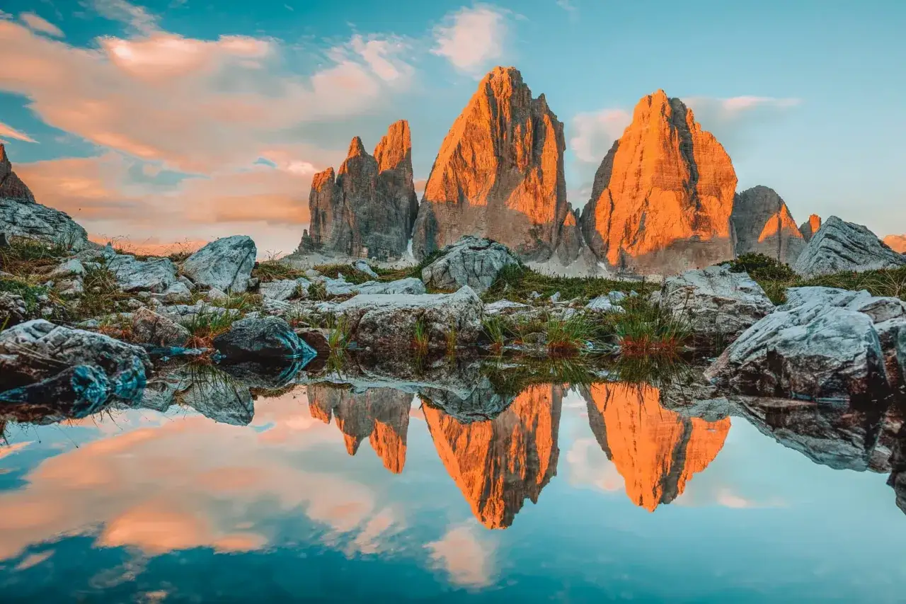 Sonnenuntergang über den Drei Zinnen, ein ikonisches Ziel für fernwanderwege italien. Die Berge spiegeln sich in einem ruhigen Bergsee.