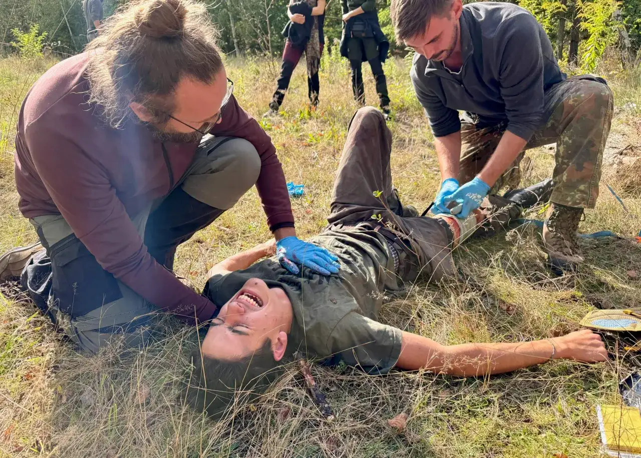 Erste Hilfe bei einem Sturz im Wald. Ein Mann mit einem Rippenbruch wird von zwei Helfern versorgt.