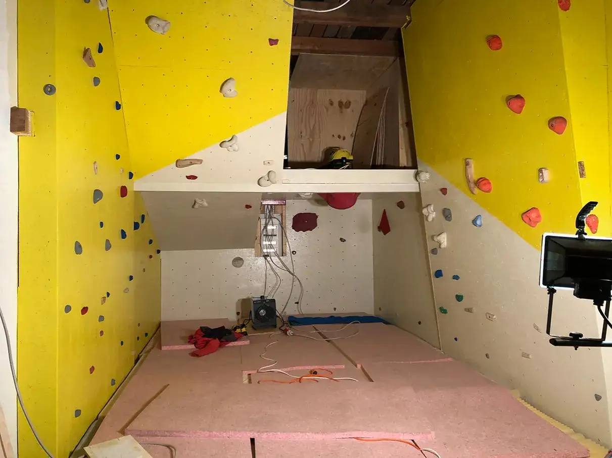 Ein Raum wird zum Kletterparadies: Gelbe und wei&szlig;e W&auml;nde mit Griffen, der Boden ist mit rosa Matten ausgelegt. Hier entsteht eine Boulderwand selber bauen.