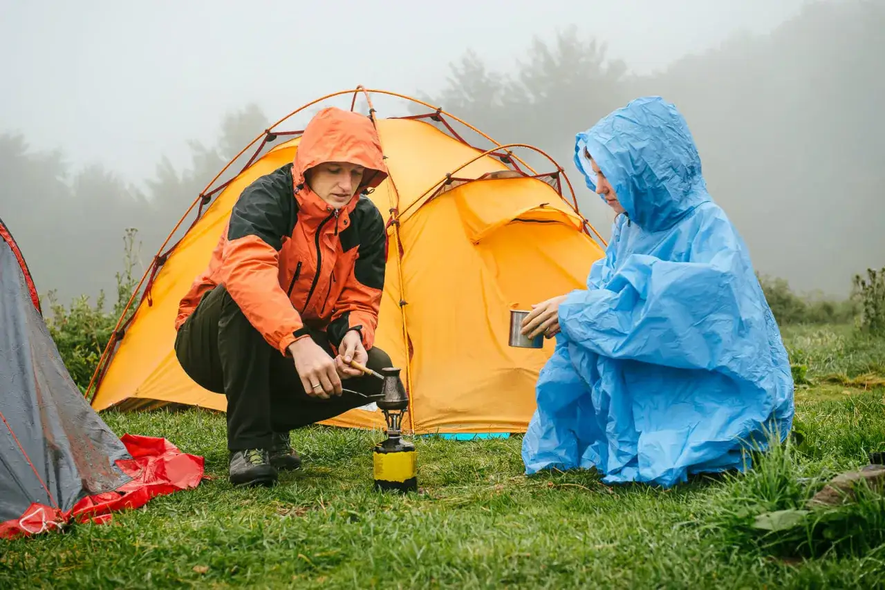 Zwei Camper bauen bei Regen ihr Zelt auf und bereiten sich eine warme Mahlzeit zu.