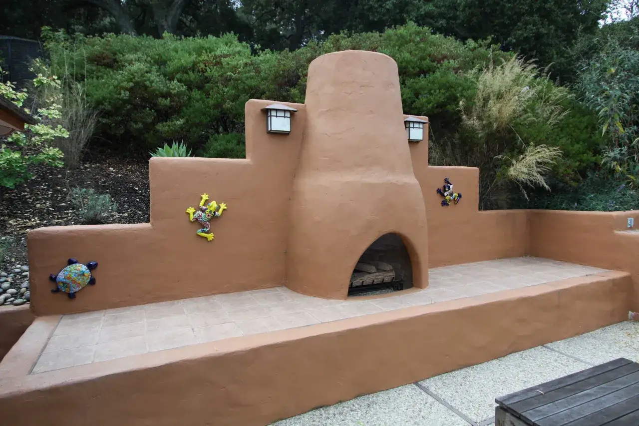 Ein rustikaler, selbstgebauter outdoor ofen mit bunten Keramik-Echsen und Schildkröten, umgeben von üppigem Grün.