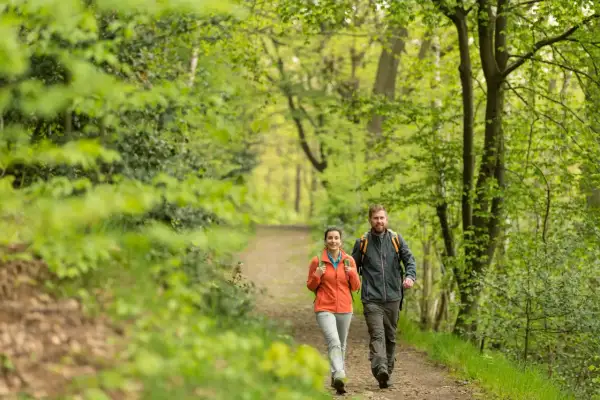 Ein Paar genießt eine Wanderung mit Einkehr im Grünen. Sie gehen auf einem Waldweg, umgeben von üppiger Vegetation.