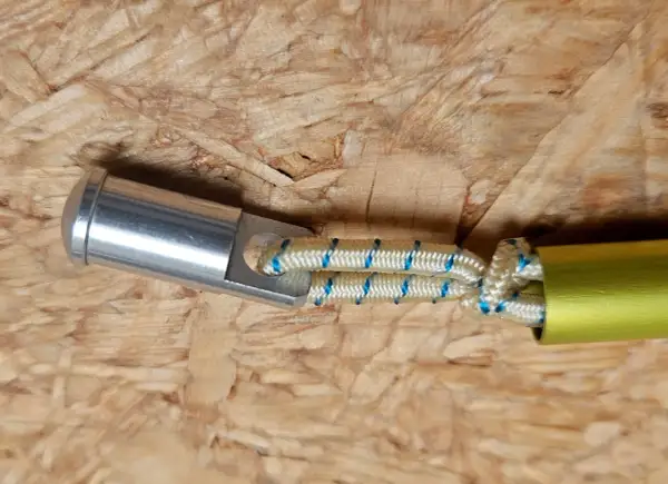 Detailaufnahme: Ein silbernes Endstück mit einer Öse ist mit einem elastischen Seil verbunden, das in ein gelbes Rohr führt. Dies ist eine Methode, um eine Zeltstange zu reparieren.