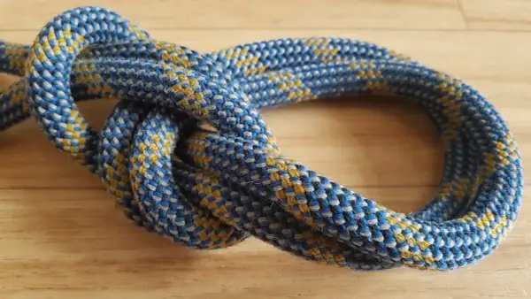 Ein blauer und gelber Seilstrang bildet einen sicheren bulin knoten auf einer Holzoberfläche.