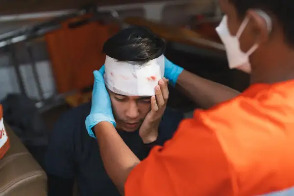 Sanitäter versorgt eine Platzwunde am Kopf eines jungen Mannes mit Verband.