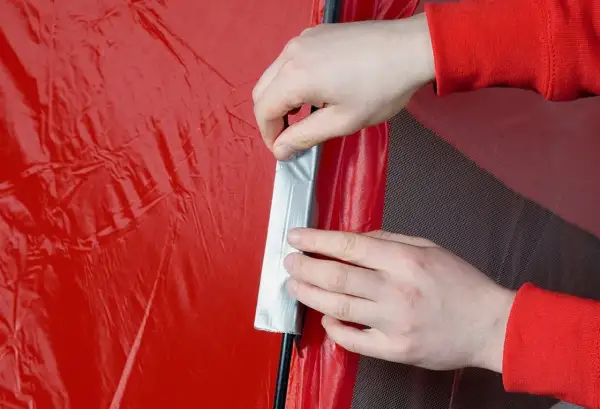 Hände reparieren mit Klebeband eine rote Zeltplane.