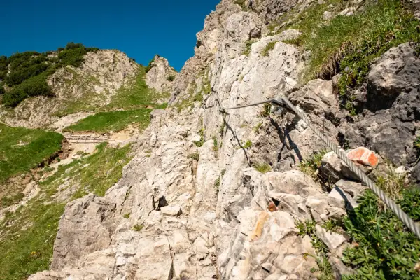 Auf einer steilen Felswand mit Seilsicherung für die rubihorn wanderung. Grüne Hänge und blauer Himmel.