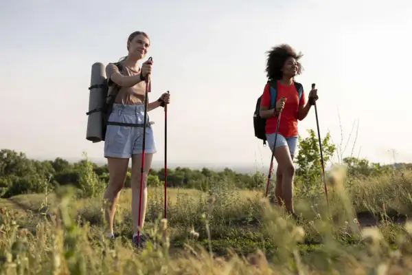 Zwei Frauen genießen eine 10 km Wanderung gesund in der Natur. Sie tragen Rucksäcke und Trekkingstöcke.