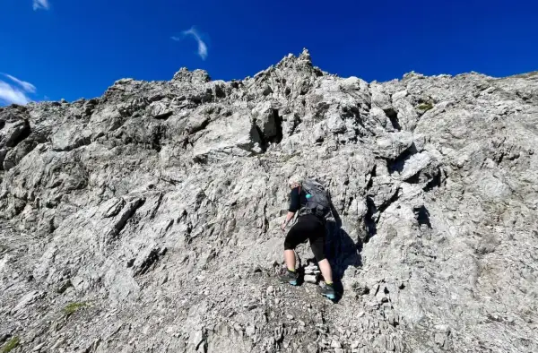 Frau klettert einen steilen Felsgrat im 3. Grad. Der Himmel ist strahlend blau.