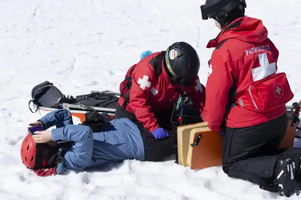 Bergretter kümmern sich nach einem Sturz auf Knie um einen verletzten Skifahrer im Schnee.