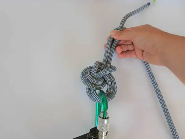 Hand hält ein Seil, das zu einem dicken Knoten gebunden ist, der an einem Karabiner befestigt ist.