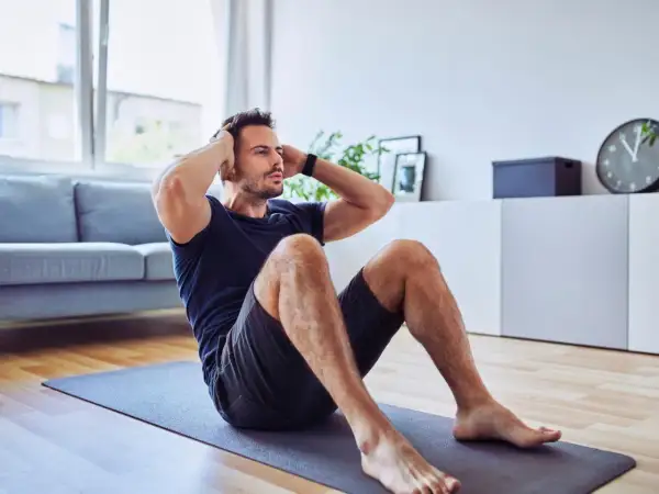 Mann macht Sit-ups auf einer Matte. Er trainiert trotz eines möglichen Rippenbruchs, um fit zu bleiben.