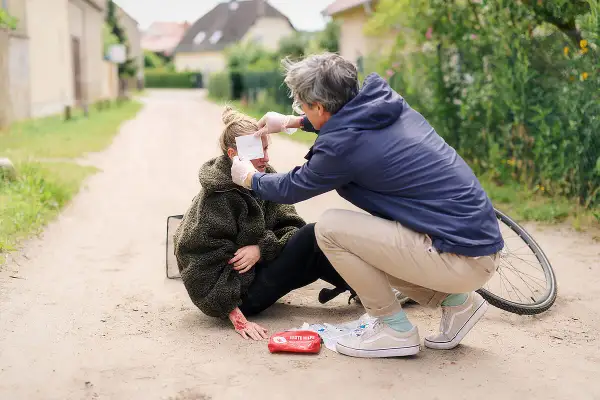 Erste Hilfe nach einem Sturz: Ein Mann versorgt eine Frau mit aufgeschürfter Hand und einem Verband am Auge.