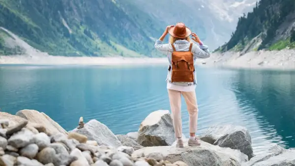 Frau mit Rucksack und Hut steht am Ufer eines türkisfarbenen Sees in den Bergen. Ein malerischer Ausblick, wie man ihn in Seen Deutschland findet.