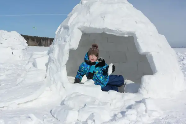 Kind im selbstgebauten Iglu, bereit für Winterabenteuer.