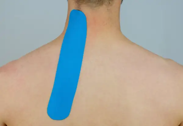 Blaues Kinesio-Tape wird am Nacken und Schulterblatt angebracht, um Unterstützung zu bieten.