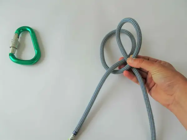 Eine Hand formt einen Knoten aus einem Seil, daneben liegt ein grüner Karabiner. Verschiedene Knoten sind wichtig für Kletterer.
