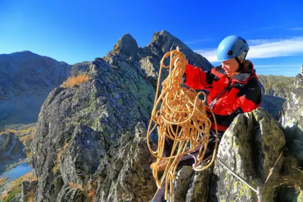Bergsteigerin mit Seil in den Bergen, bereitet sich auf das Klettern vor und achtet auf wichtige Knoten.