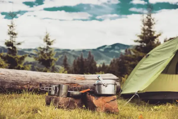 Campingausrüstung im Wald: Töpfe, Tasse und ein Zelt. Hier darf man im Wald schlafen und die Natur genießen.