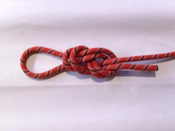 Ein rotes Seil mit schwarzen und weißen Mustern bildet einen Achterknoten, der sicher und stabil aussieht.