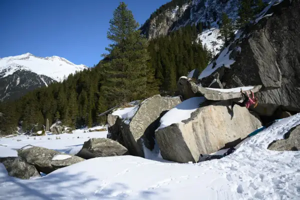 Eine Person klettert an einem Felsen im verschneiten Zillertal. Bouldern im Schnee ist eine Herausforderung!