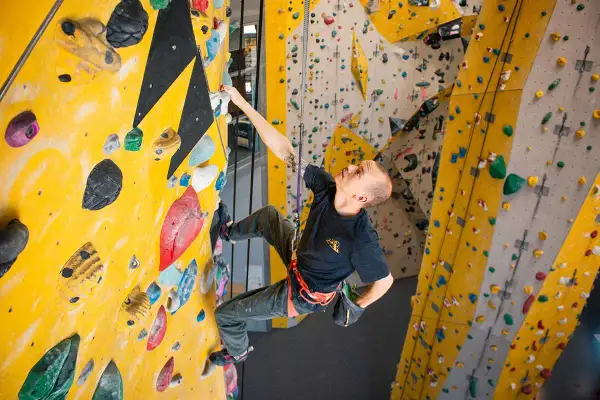 Mann klettert an einer gelben Wand mit bunten Griffen. Verschiedene klettern arten sind hier möglich.