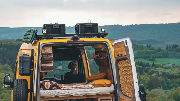 Gelbes Campervan mit gemütlichem Innenraum, bereit für wildcampen in Europa. Dachgepäckträger, Ersatzrad und Stauraum für Abenteuer.