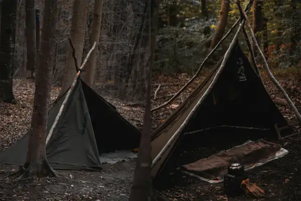 Zelt aufbauen Anleitung: Ein Tipi-Zelt aus Stoff, gestützt von Ästen, im Wald. Innen liegen Decken und eine Teekanne.